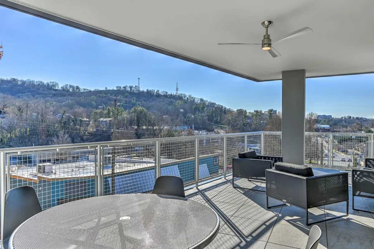 An outdoor seating area featuring a table and chairs, set against a backdrop of rolling hills. The space looks perfect for relaxing or socializing, with sweeping views that hint at the beauty of the surrounding Asheville area. The design invites guests to enjoy the fresh air and serenity, perhaps after a day exploring local attractions.