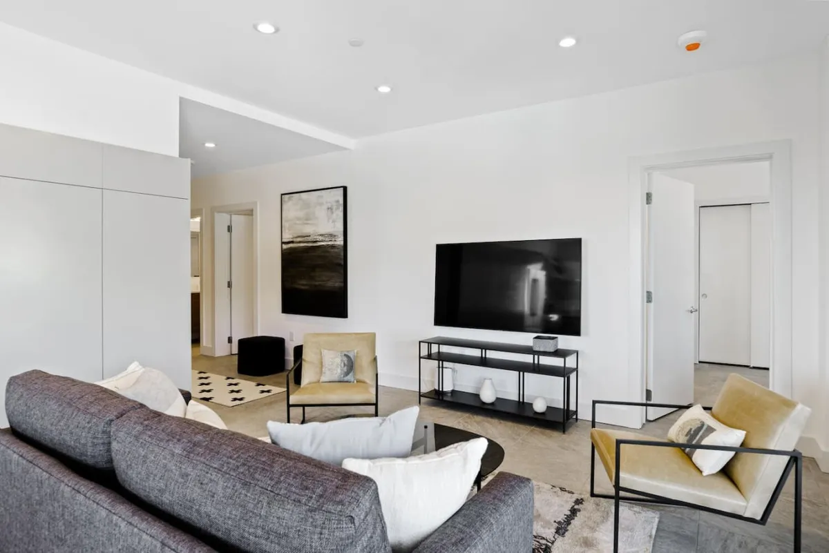 A contemporary living room with a plush sofa, armchairs, a television, and vibrant artwork. The setup is conducive to casual gatherings, movie nights, or simply unwinding after exploring Asheville. The furniture is arranged to create a warm, inviting environment ideal for guests and their pets to relax together.