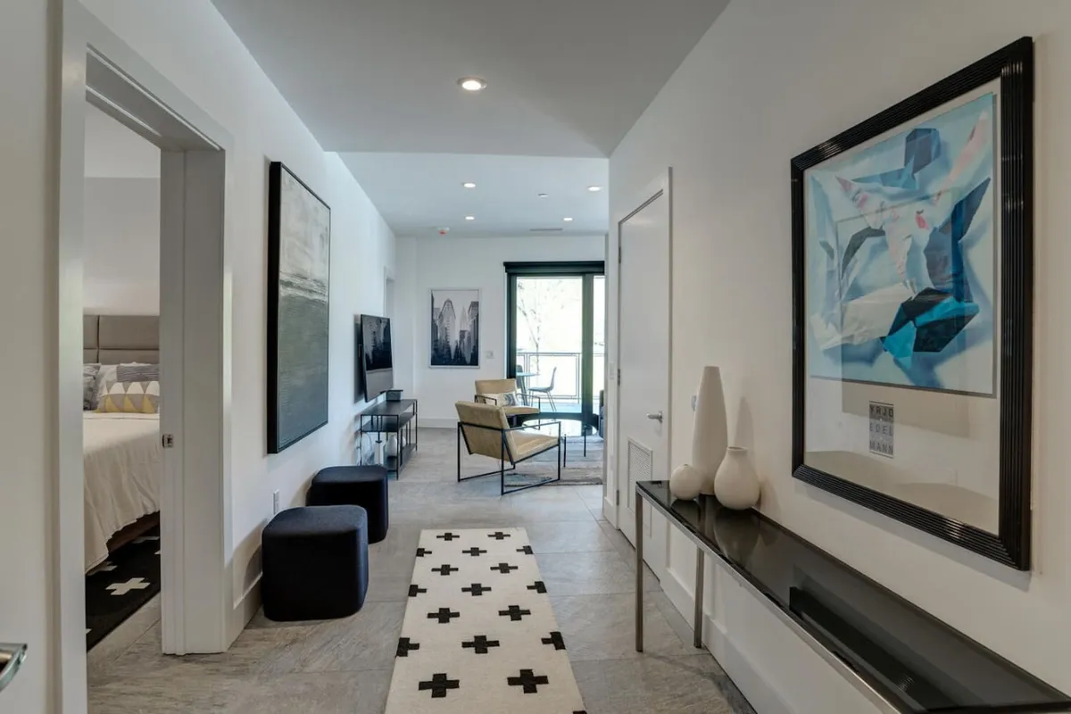 A modern, stylish seating area with contemporary artwork on the walls, decorative vases, and a geometric patterned rug. Sunlight pours through the windows, creating a welcoming space for conversation, relaxation, or gathering with family after a day out.