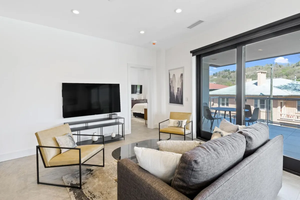 A stylish living room with a plush sofa, armchairs, a coffee table, TV, and large windows, offering space for relaxation, entertainment, and enjoyment of the view. The setting is modern yet comfortable, catering to group gatherings or quiet leisure.