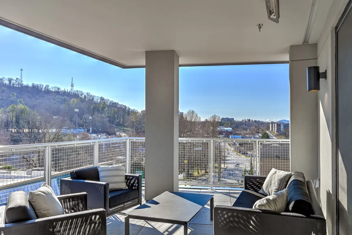 An exterior shot featuring a cozy seating area and a scenic vista over the neighborhood. The view includes both natural landscape elements and a hint of city life below, suggesting a vantage point where one can observe Asheville’s energetic street culture while relaxing at home.