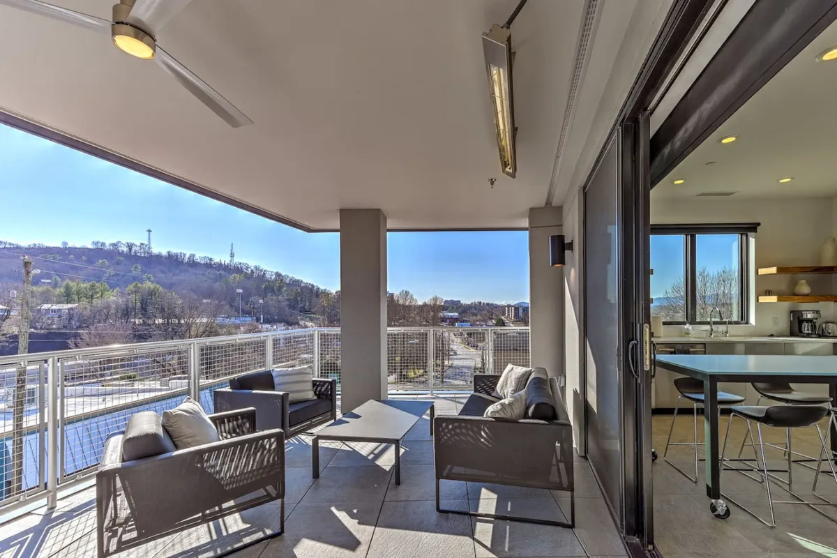 An outdoor seating area on a private balcony, complete with comfortable chairs and panoramic city views. The kitchen interior is visible through the glass, emphasizing the seamless flow between inside and outside. This space is ideal for relaxing, enjoying drinks, and taking in the urban landscape.