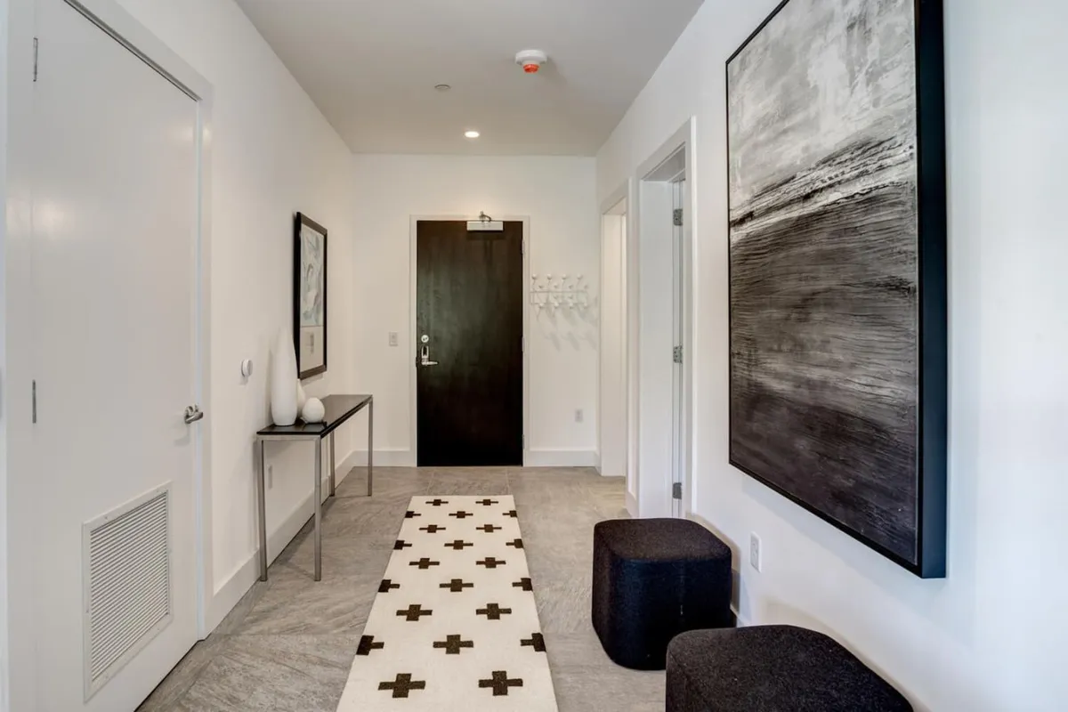 A stylish entryway featuring black and white artwork, a geometric patterned runner rug, and a dark wooden door. The space presents a welcoming environment for returning from city walks or bringing in your pet. The contemporary design sets the tone for refined urban living.